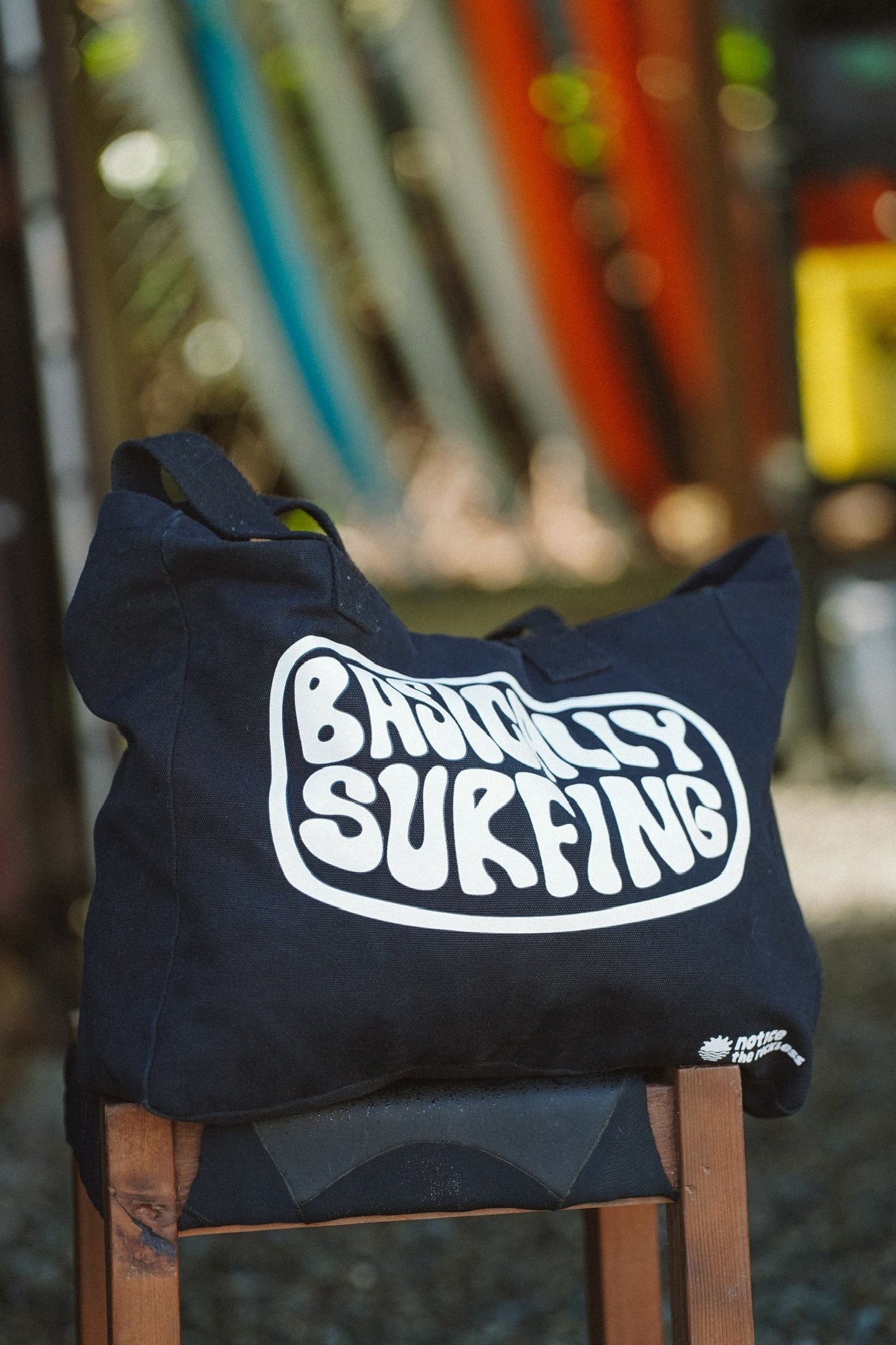 Black cotton canvas beach tote bag featuring bold front print, durable wide straps, inside zipper pocket and relaxed summer style ideal for beach trips and daily adventures