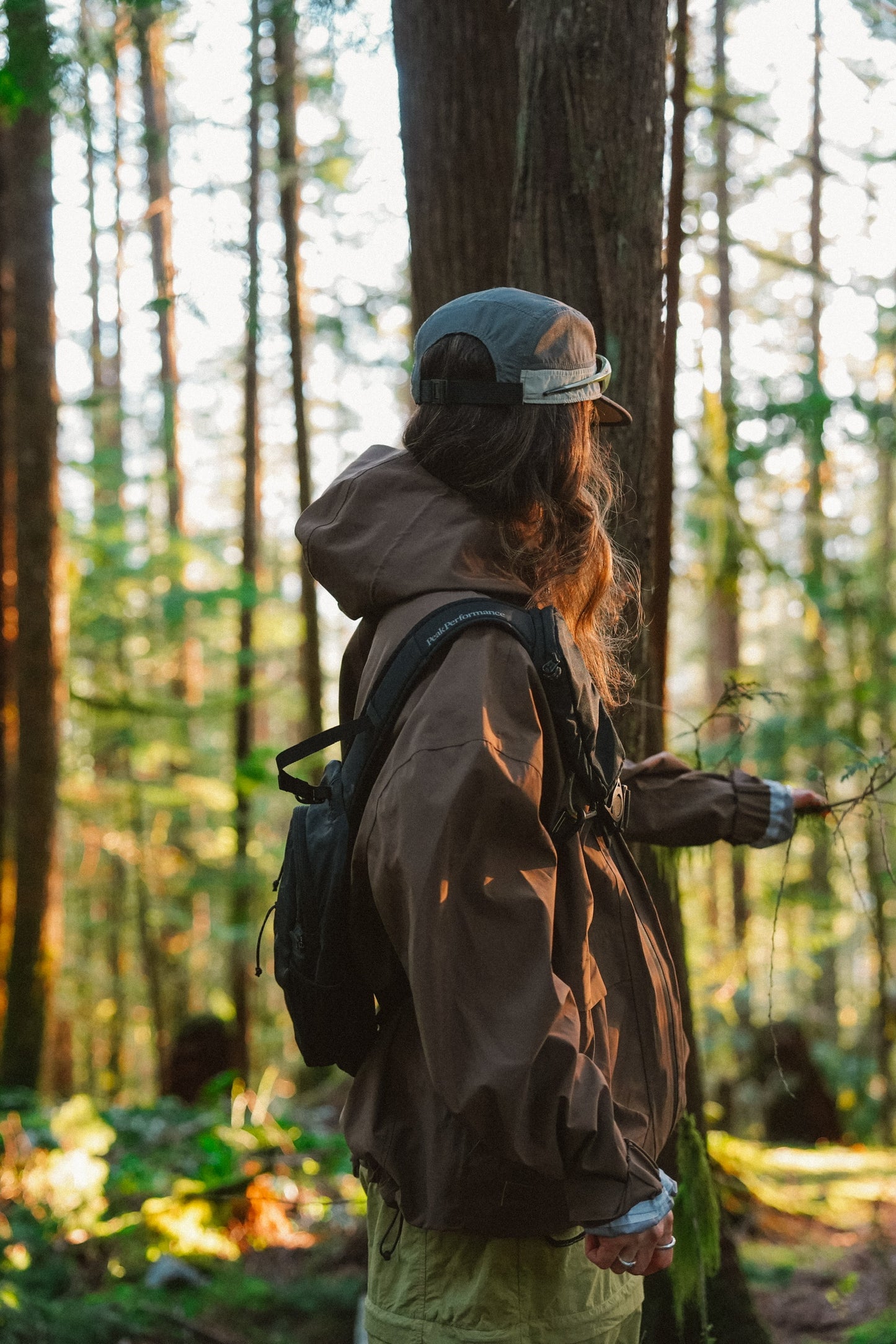 Woman wearing espresso brown hooded waterproof hiking rain jacket with adjustable hood in the woods