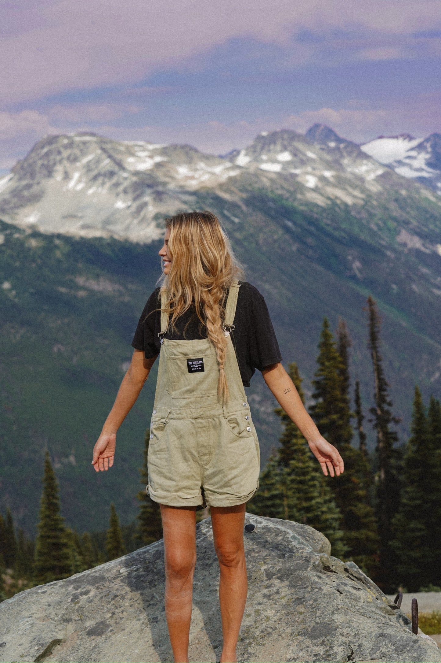Woman wearing sage green cotton overalls in a mountain look