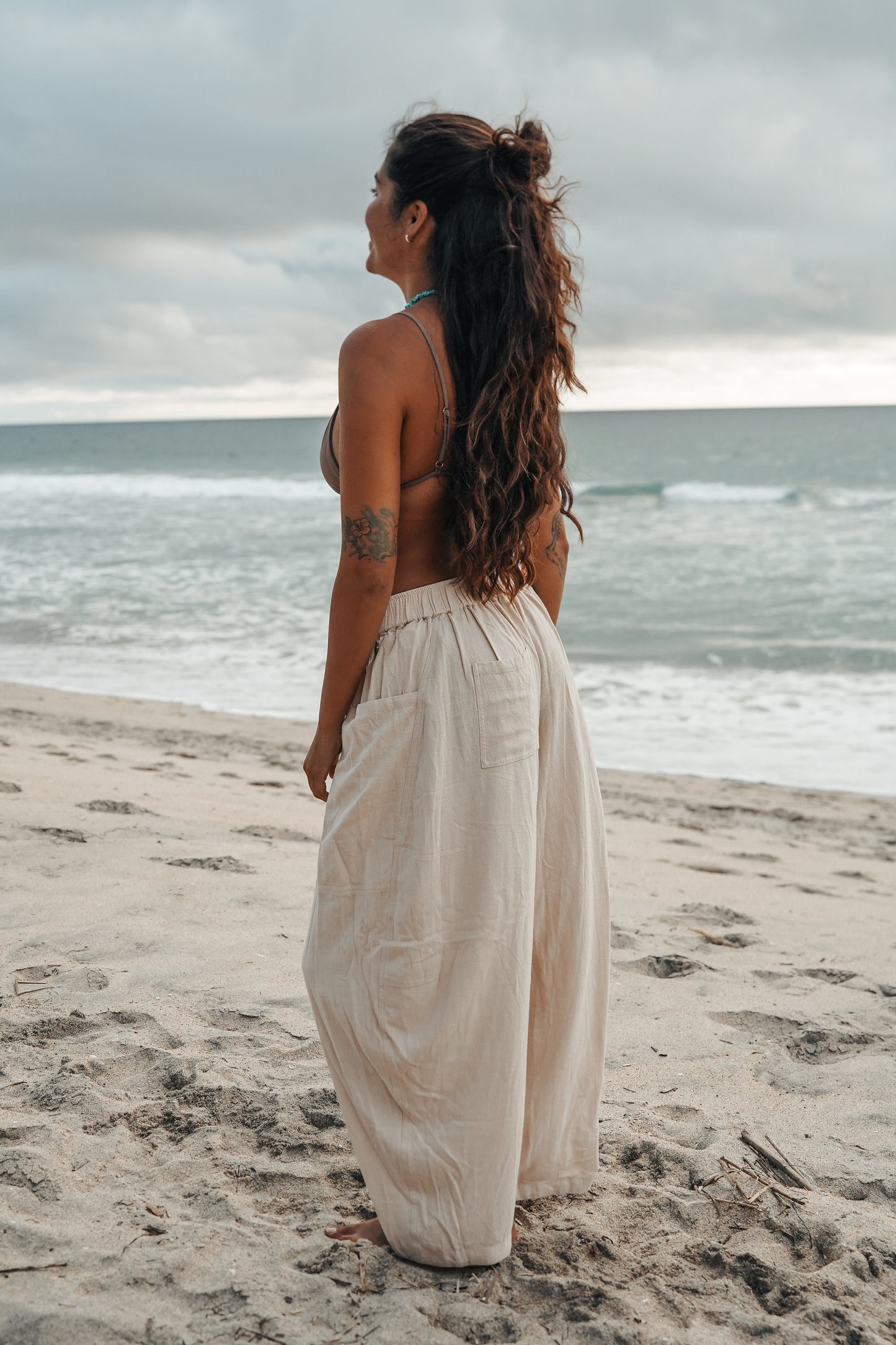 Women's sand-colored linen barrel pants with a relaxed wide-leg silhouette, elastic waistband and oversized side pockets, styled on the beach