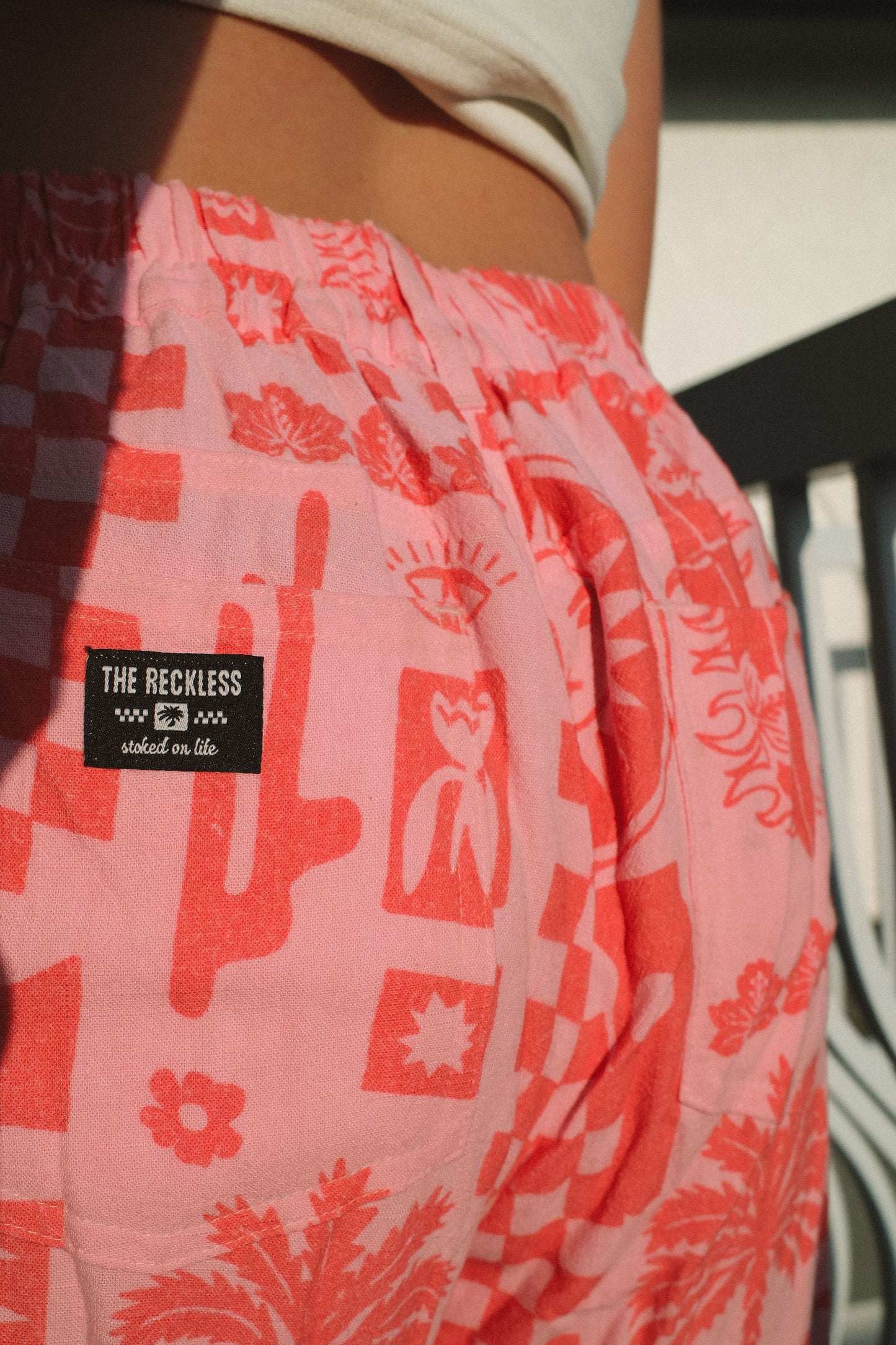 Pink and red linen shorts with a bold graphic print, zip fly with button closure, side pockets and back pockets, styled for a laid-back coastal vibe