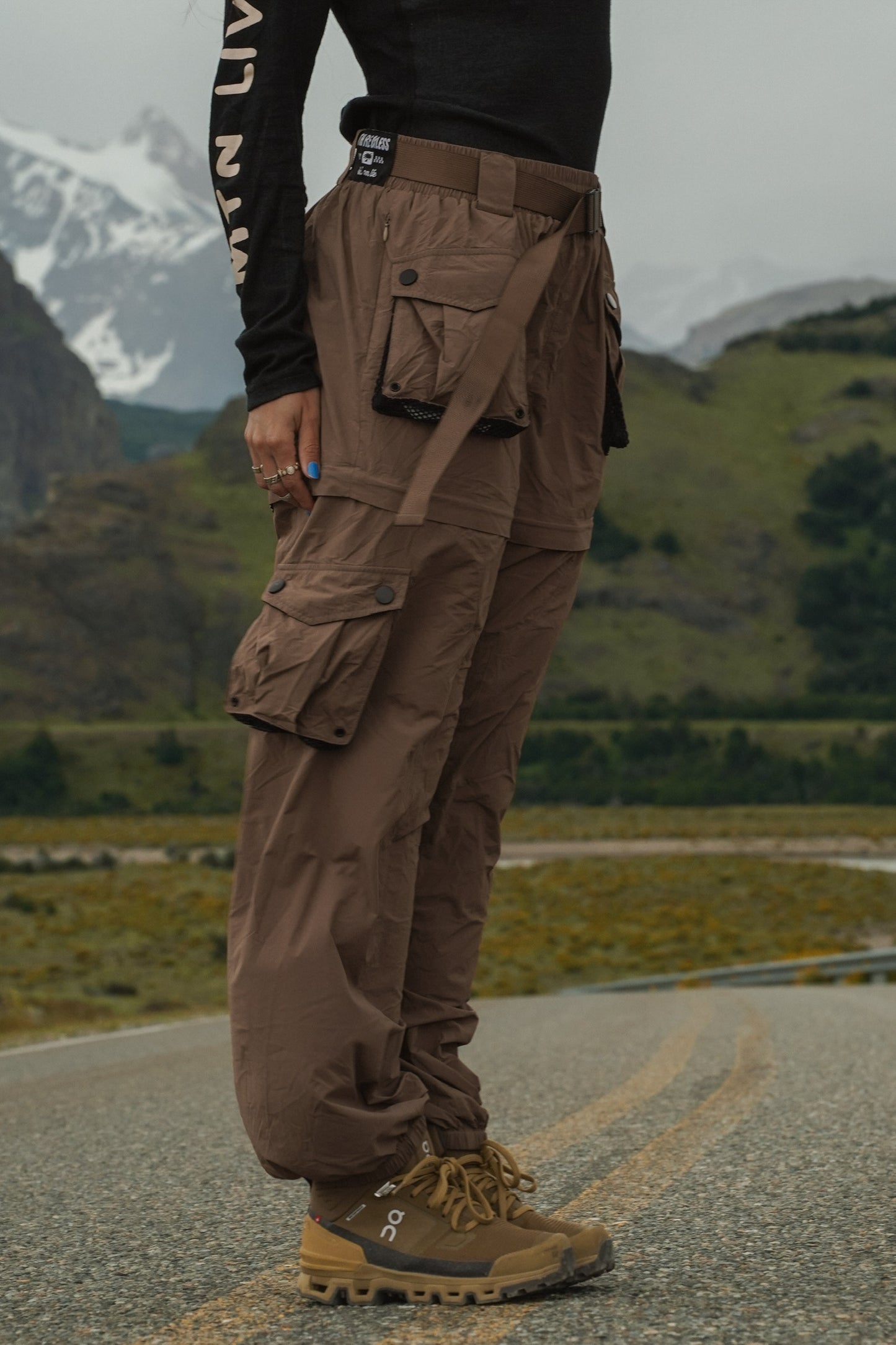 Women's walnut zip-off hiking pants with cargo pockets shown from the side on a mountain road